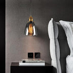 Calia Suspension Cloche en Verre, Douille Laiton – suspension en verre fumé près d'un mur gris et de coussins