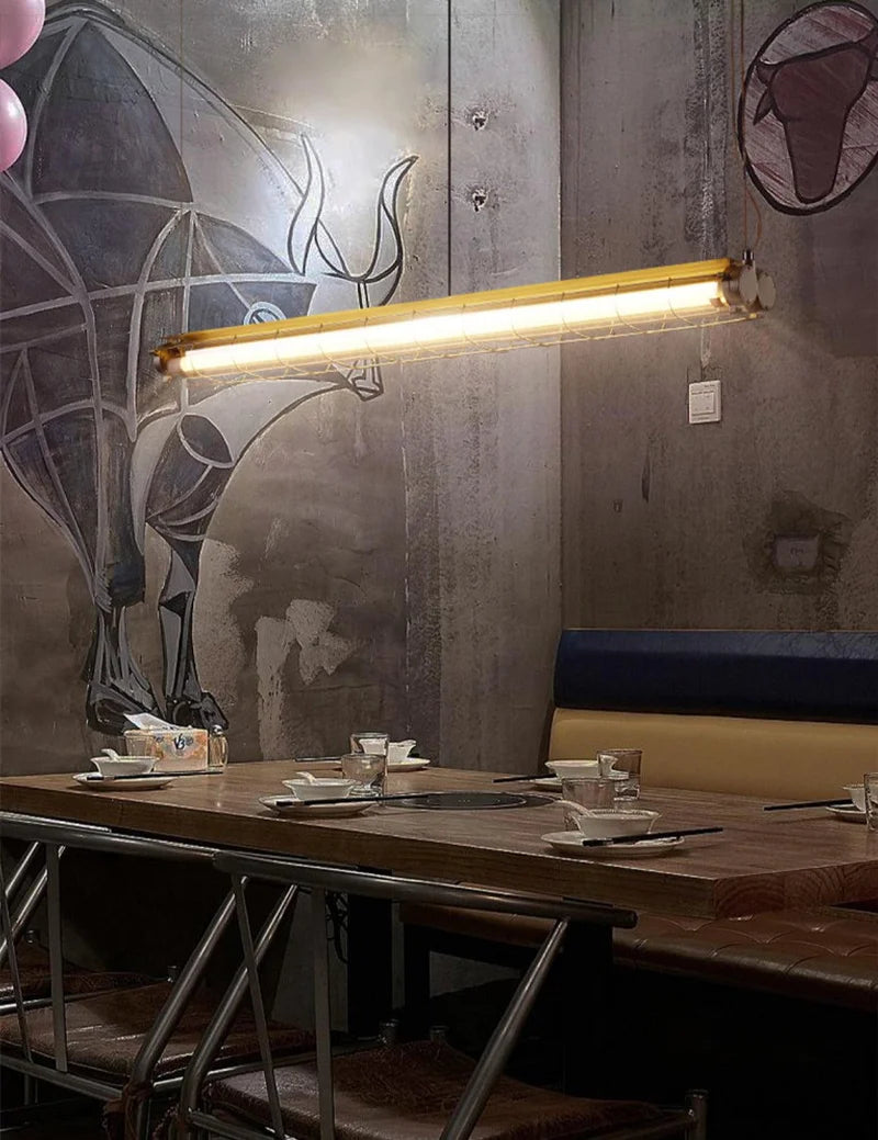 Tubia Suspension Tube en Verre Style Industriel – tube au-dessus d'une banquette bleue, mur en béton