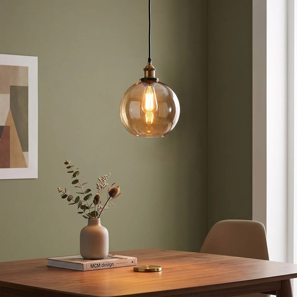 Orvane Suspension Globe en Verre, Douille Laiton – globe ambré devant un mur vert avec fleurs séchées