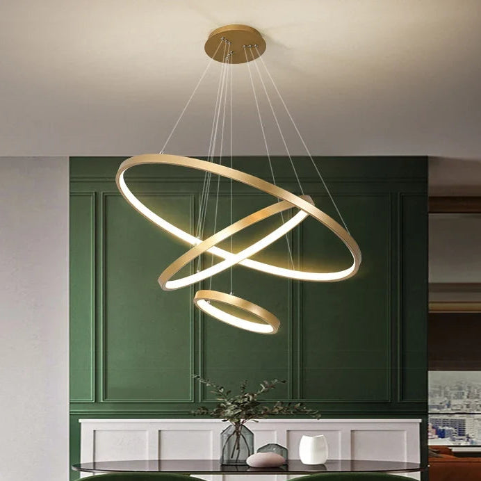 Orbite Suspension LED à Anneaux – anneaux dorés devant un mur vert à moulures