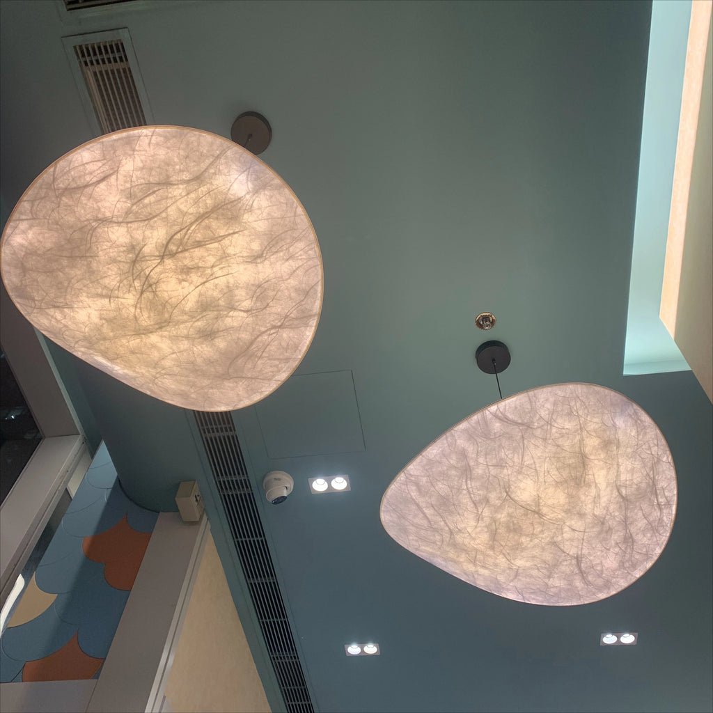 Silvane Suspension Pétales Effet Soie – deux abat-jours en forme de pétale allumés devant un mur bleu-vert