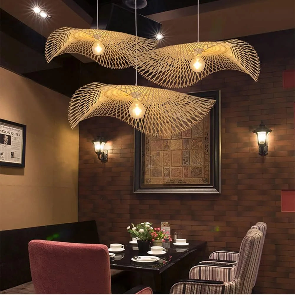 Ondine Suspension Vague Double en Bambou Tressé – devant un tableau et un mur de briques sombres