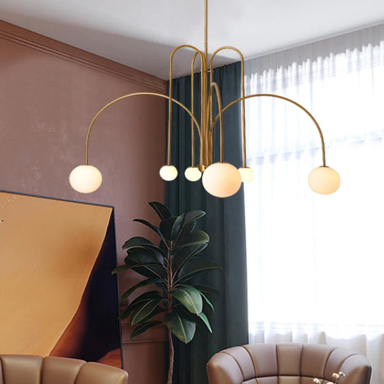 Arcadie Lustre à Bras en Arc – version dorée devant un mur rose et une plante