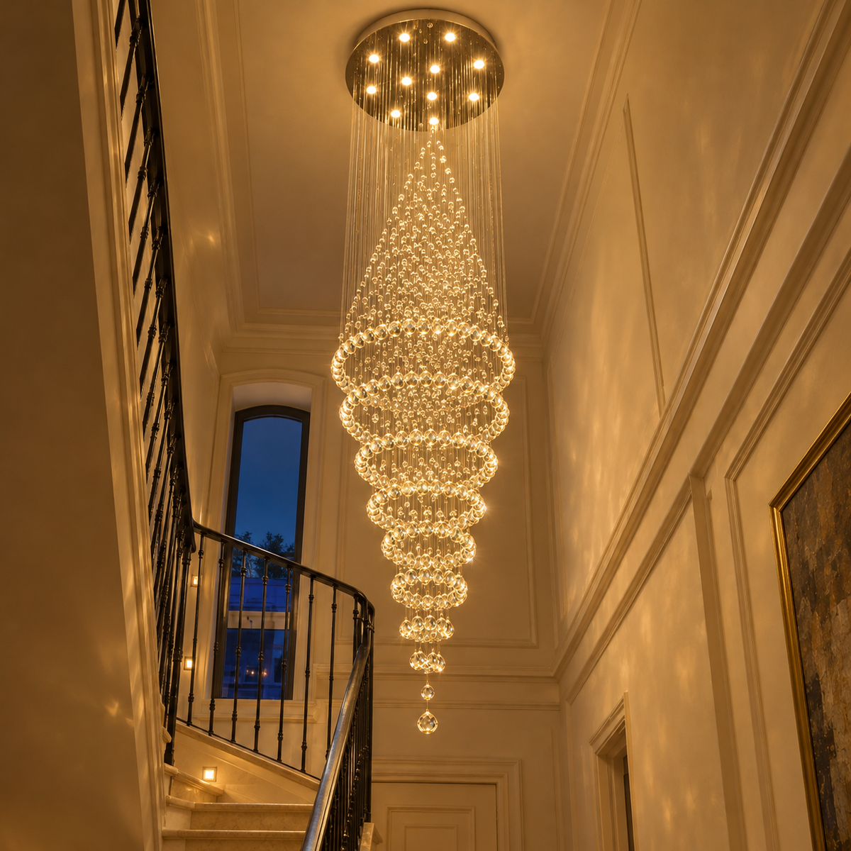 Lustre cascade en cristal allumé en soirée, lumière chaude dans l'escalier