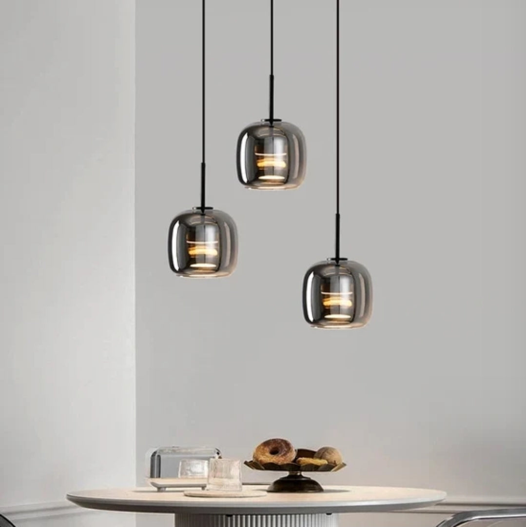 Trilia Suspension Trio en Verre, Ambré ou Fumé, sur Platine Ronde – trois suspensions en verre fumé devant un mur gris