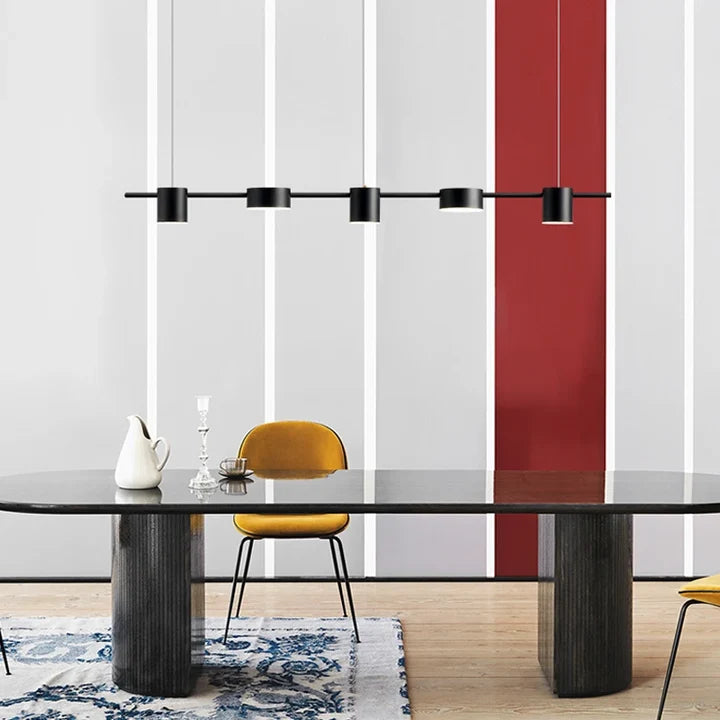 Tubo Suspension Linéaire à Spots – version noire au-dessus d'une table sombre et d'un panneau rouge